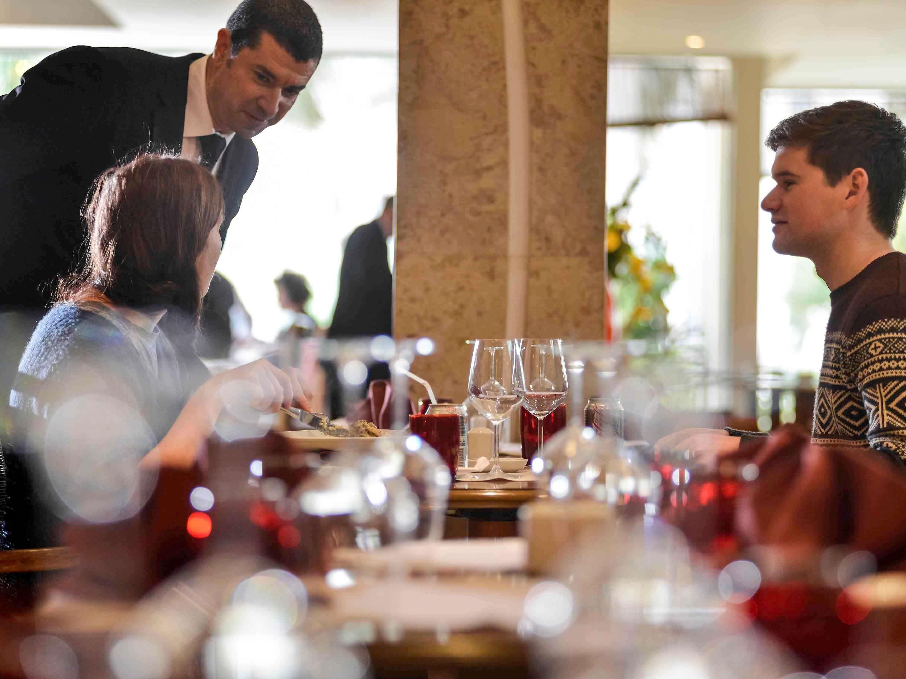 A restaurant setting with a table set for two, glasses, and a waiter attending to the guests.