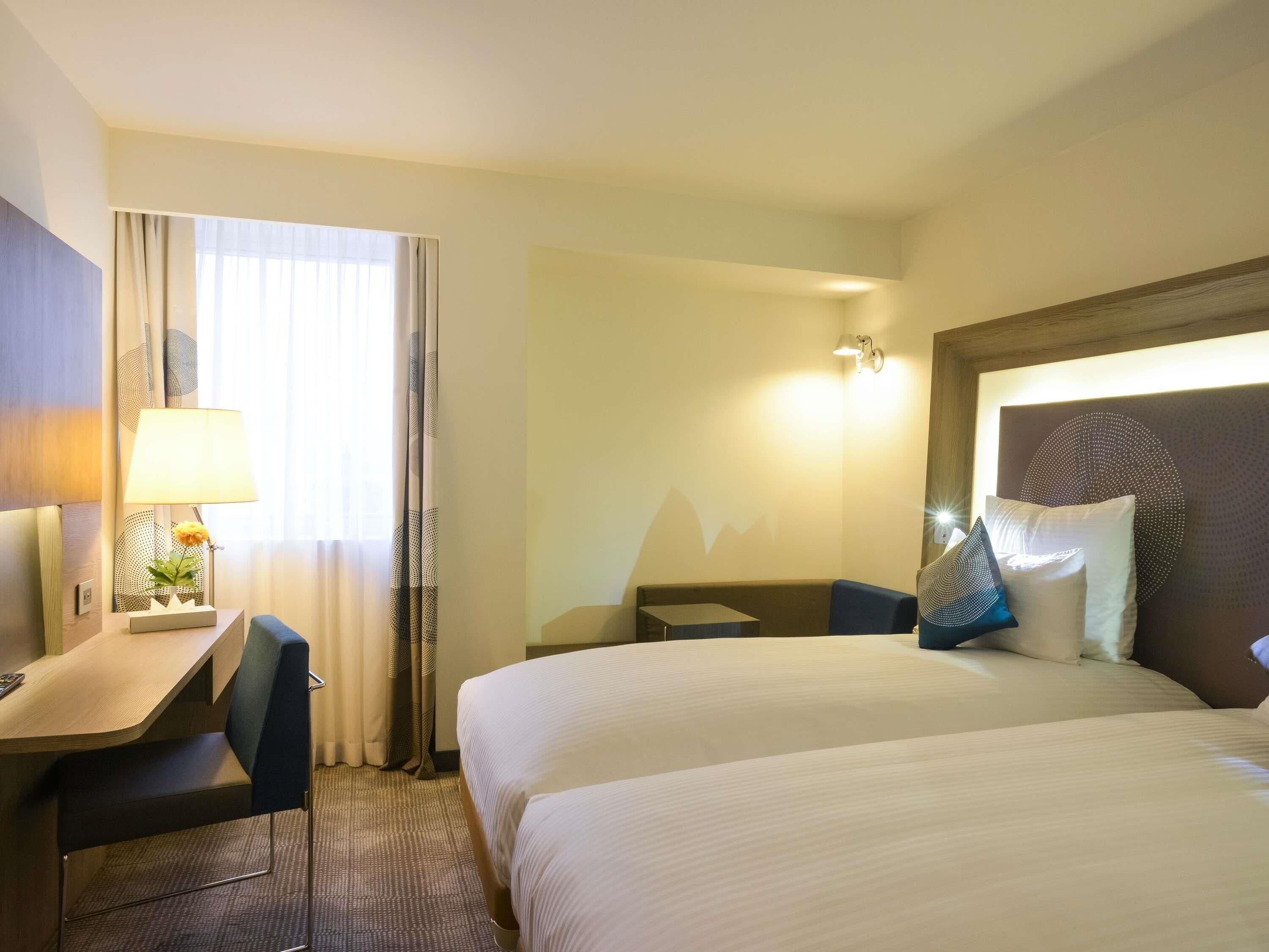 Habitación de hotel con cama, escritorio, silla, lámpara y luz en la pared.