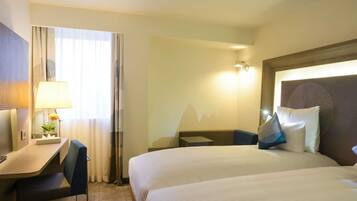 Habitación de hotel con cama, escritorio, silla, lámpara y luz en la pared.