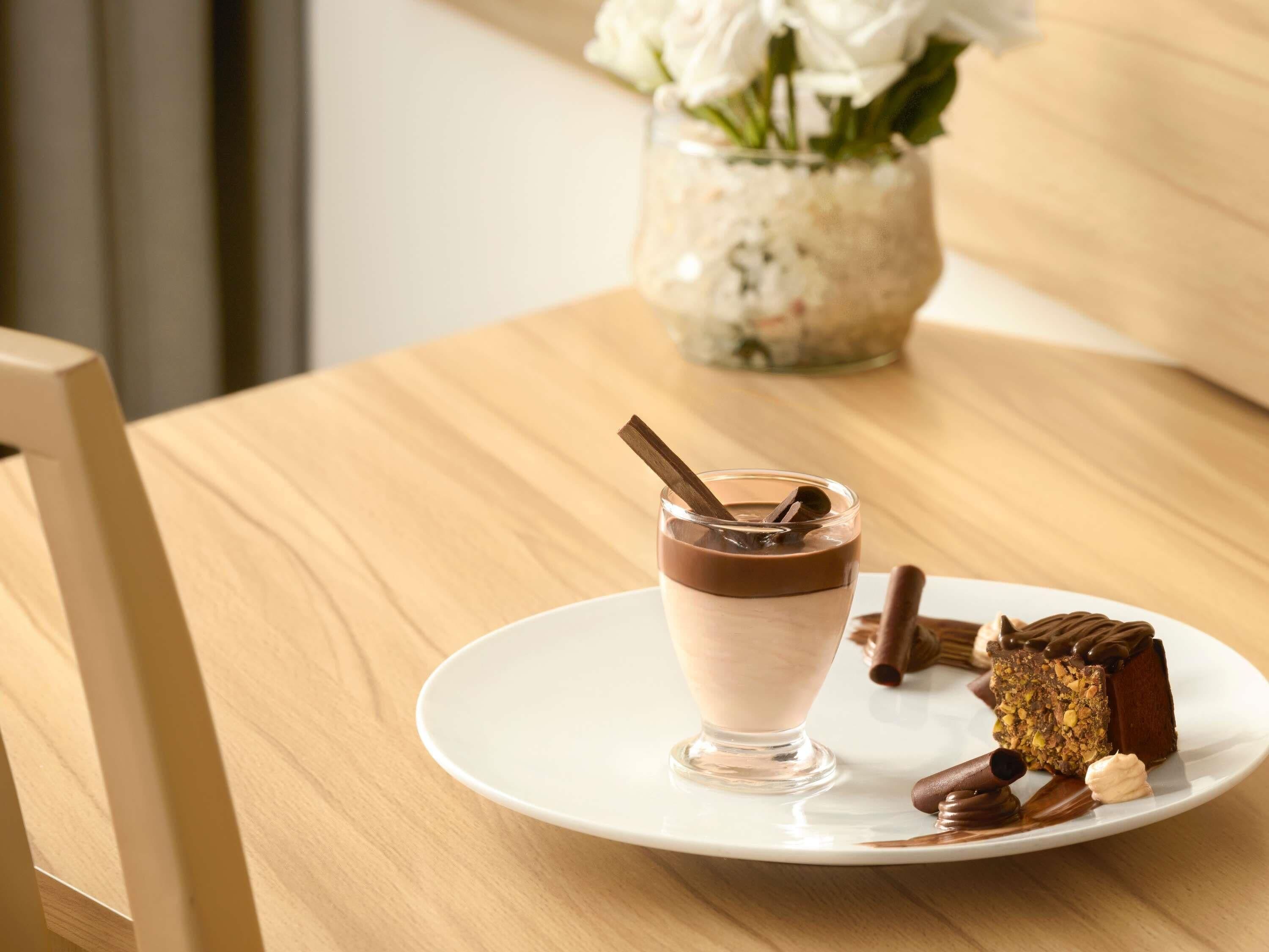 Une assiette de dessert avec une mousse au chocolat, une part de gâteau et un biscuit enrobé de chocolat, le tout présenté sur une assiette blanche.