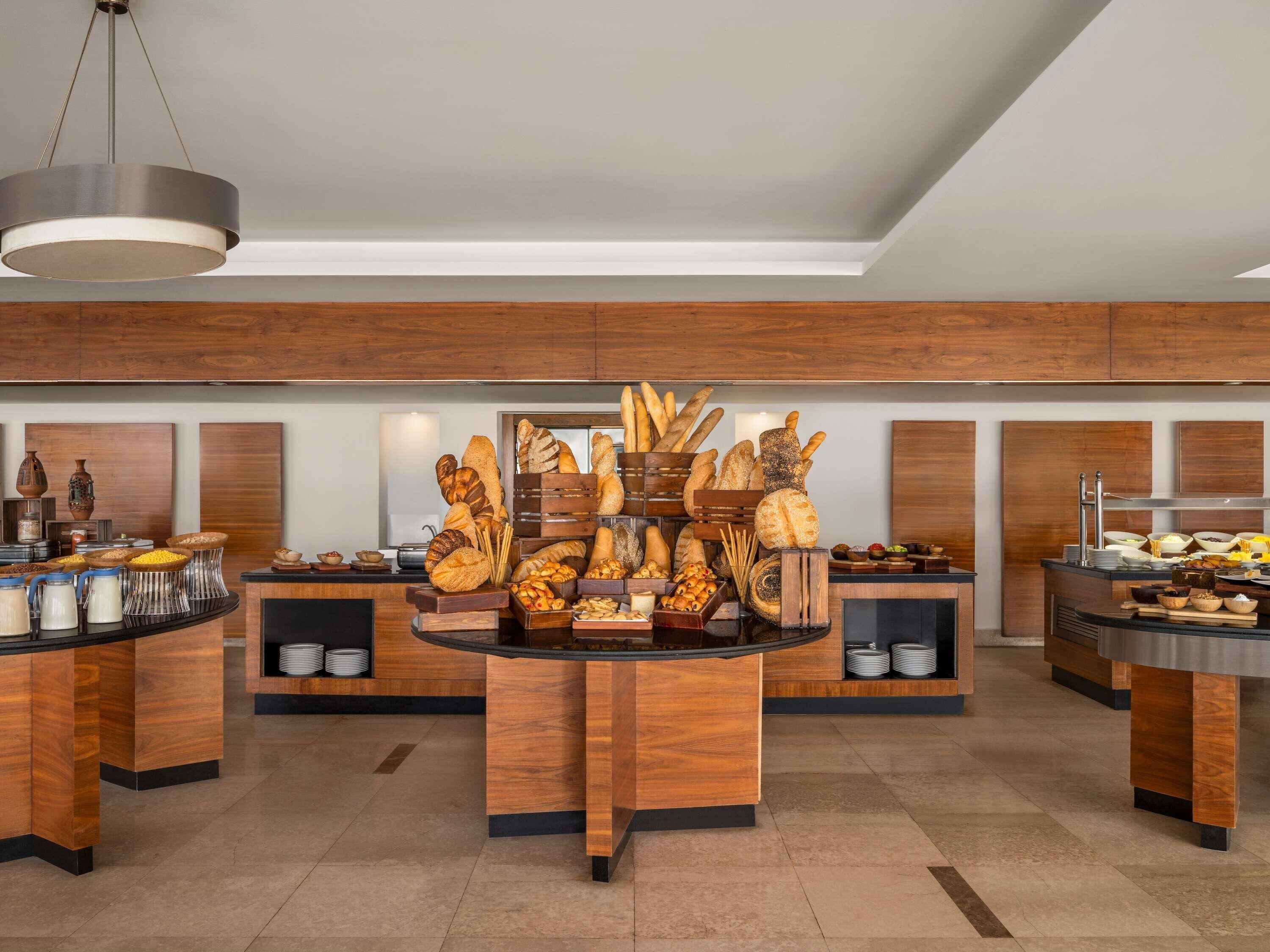 A modern kitchen with wooden cabinetry, a central island with bread, and various food items.