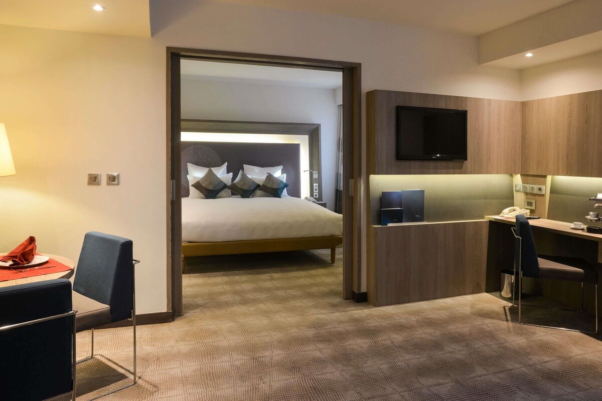 A hotel room with a bed, a desk, a chair, a TV, and a mirror.