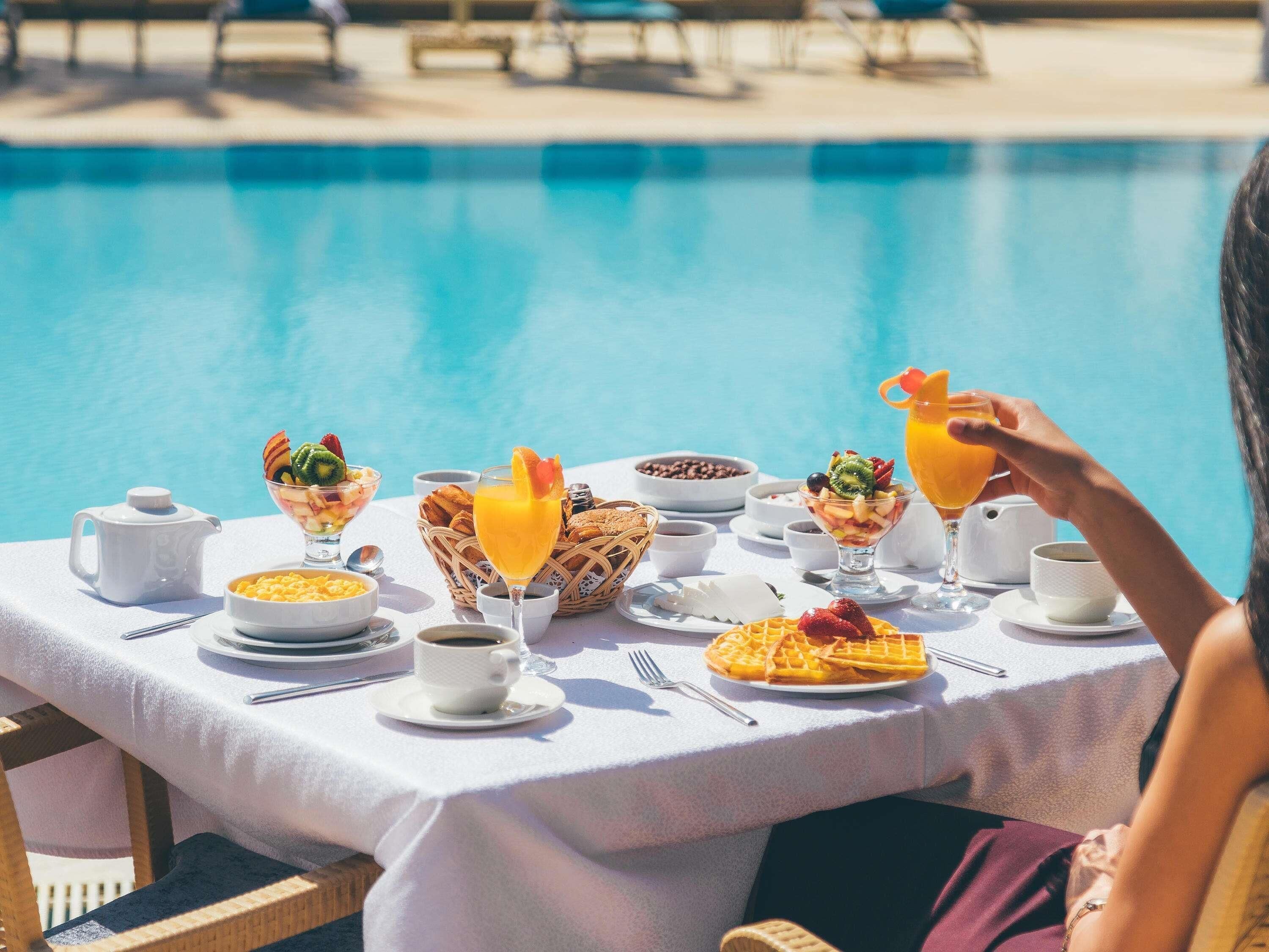 A dining table with breakfast items and a pool in the background.