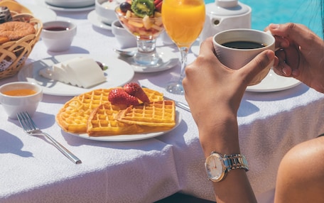 A table with breakfast items including waffles, fruit, and coffee, set by a poolside.