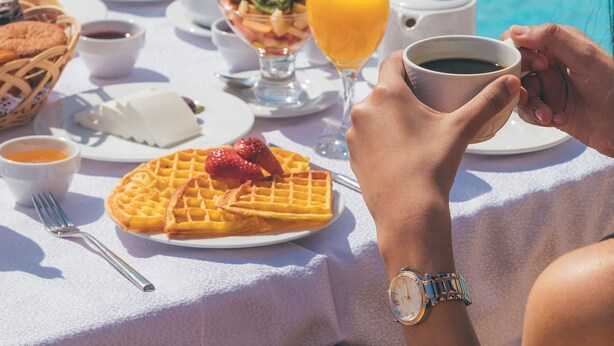 A table with breakfast items including waffles, fruit, and coffee, set by a poolside. - Novotel Cairo Airport (Cairo)