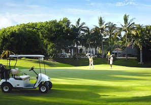 A golf course with a golf cart and a player preparing to putt.