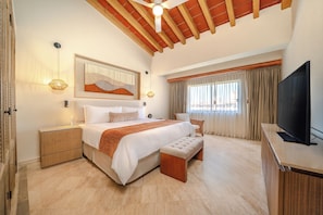 A spacious bedroom with a large bed, a television, and a ceiling fan.