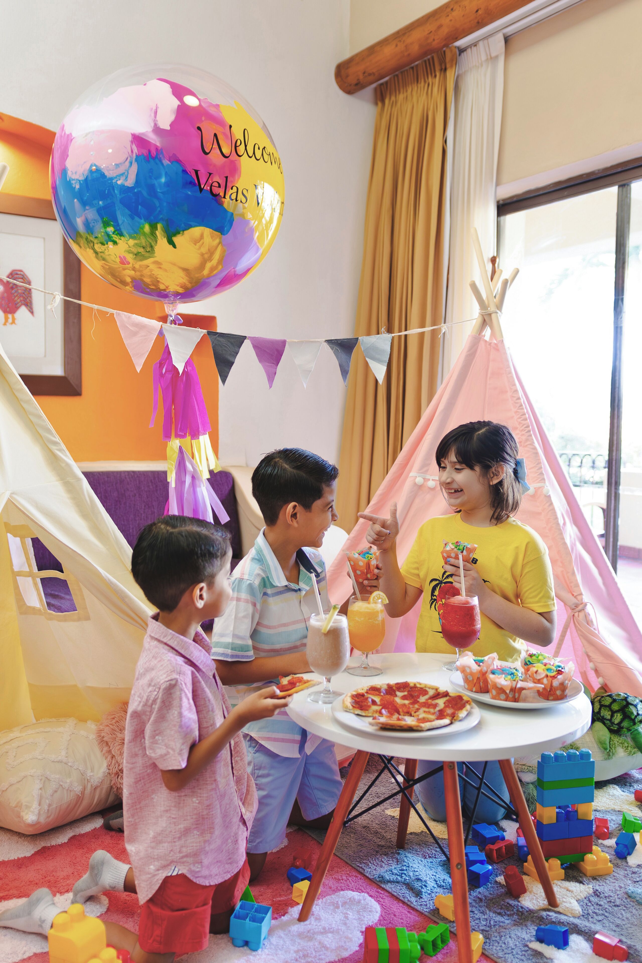 Een kamer met een witte tafel, kleurrijke ballonnen, een tent en kinderspeelgoed.