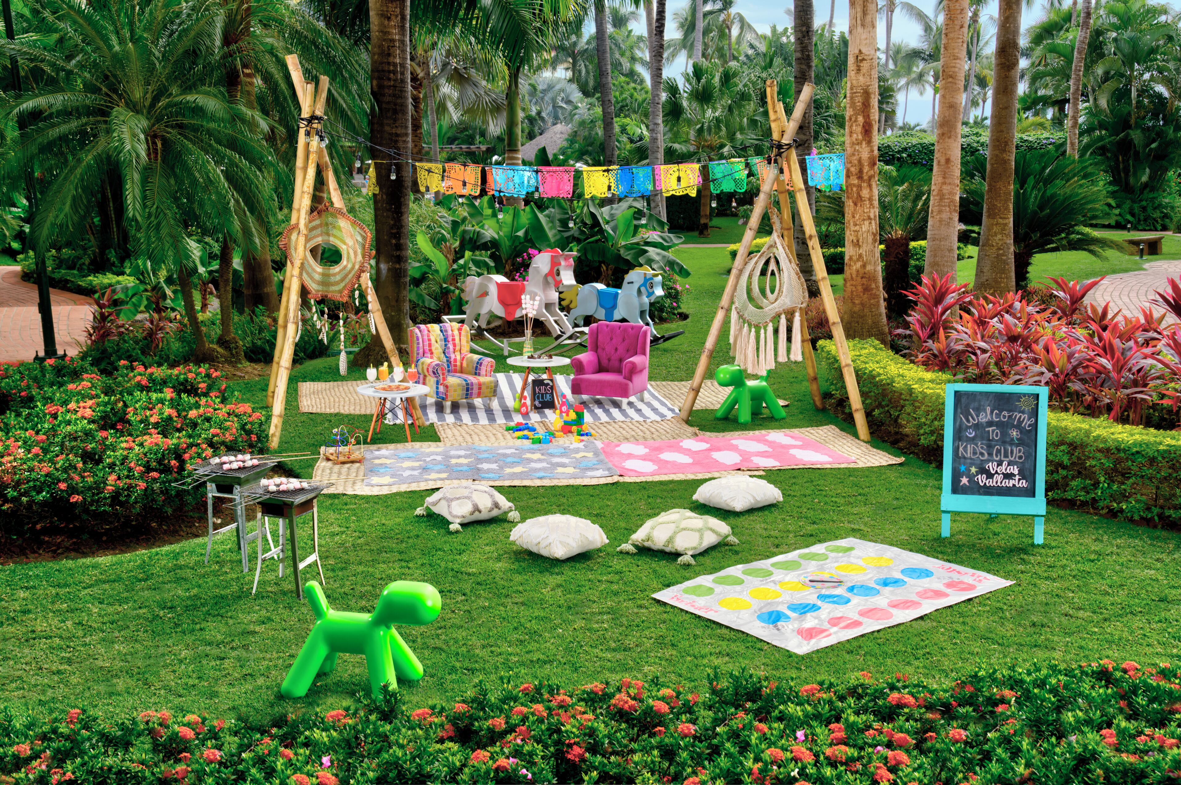 A garden with a play area, including a swing set, a teepee, and a table with toys.