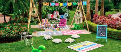 A garden with a play area, including a swing set, a teepee, and a table with toys.