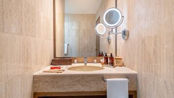 Un baño con un lavabo de mármol color beige, dos espejos redondos con iluminación, artículos de aseo y un perchero para toallas.