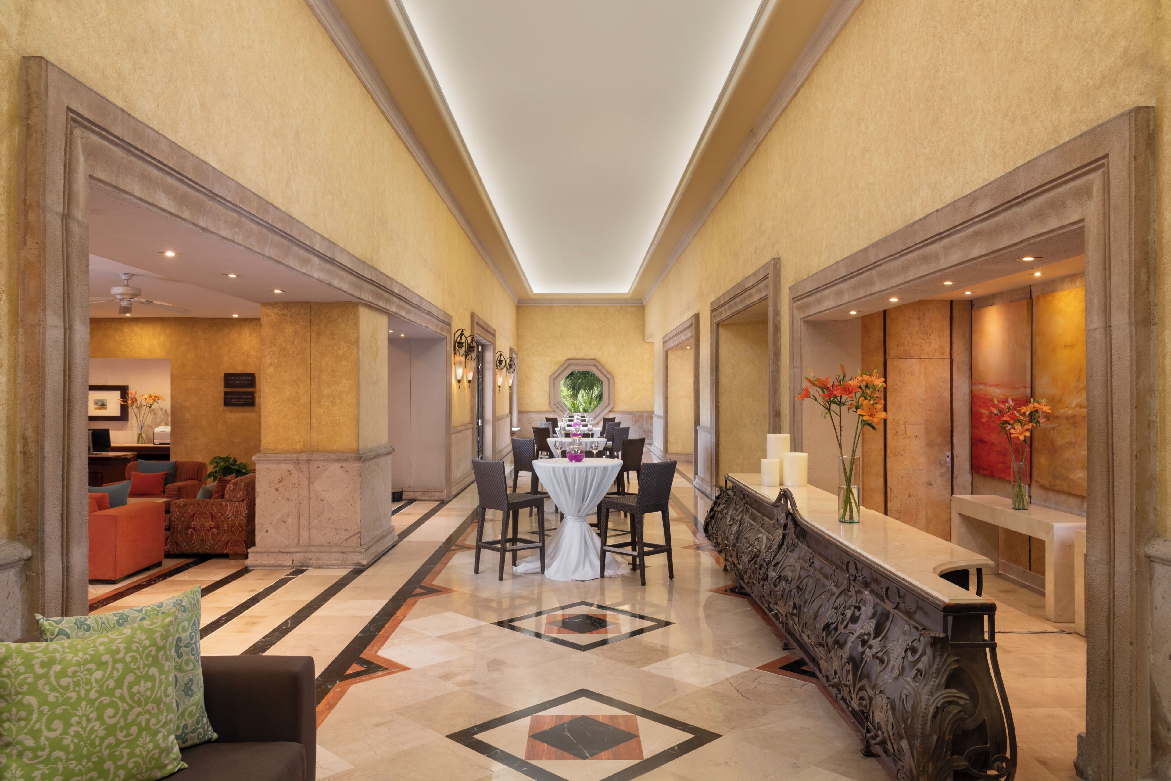 A hotel lobby with a central dining table, seating, and a decorative bench.