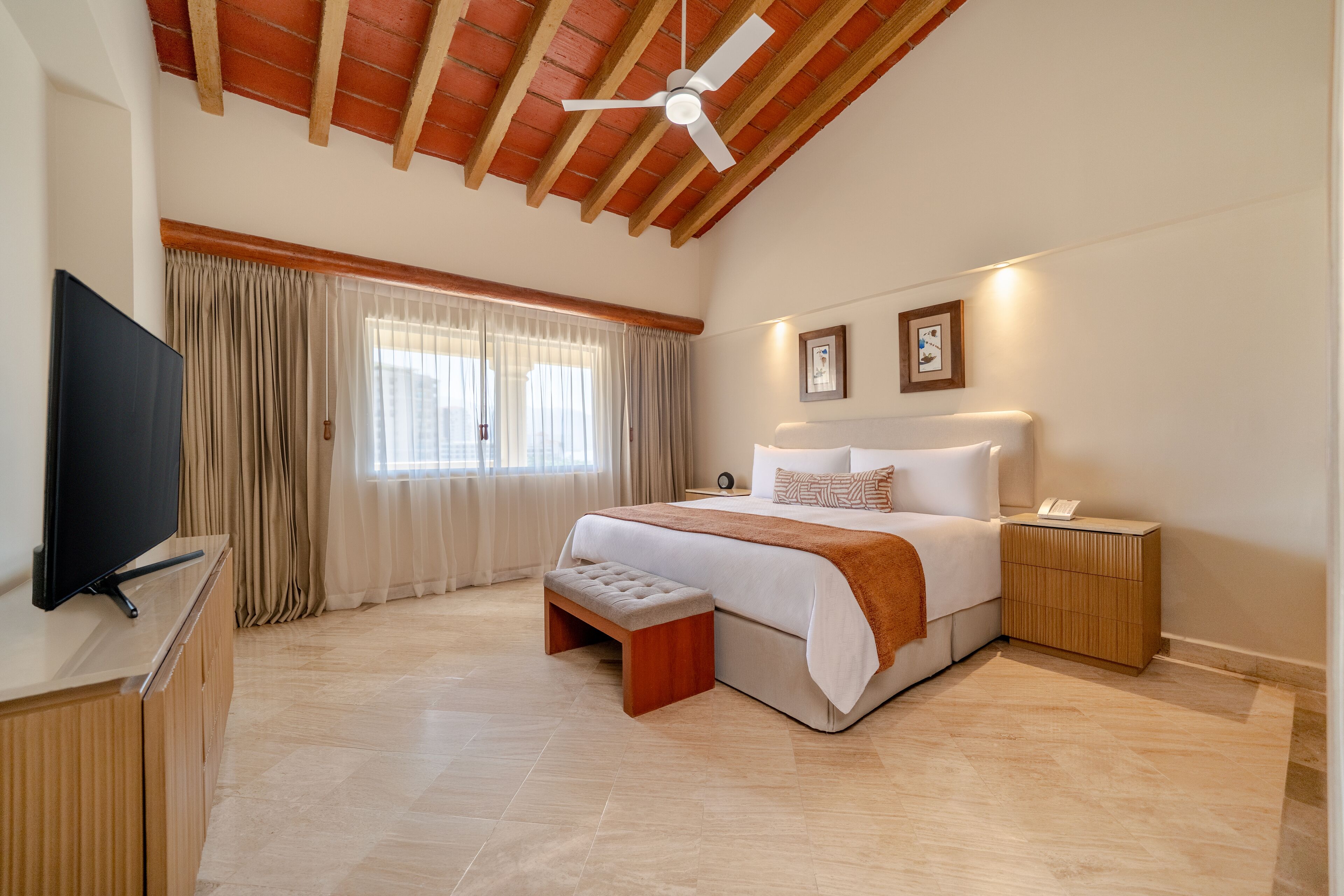 A bedroom with a bed, a TV, a ceiling fan, a bedside table, and a nightstand.