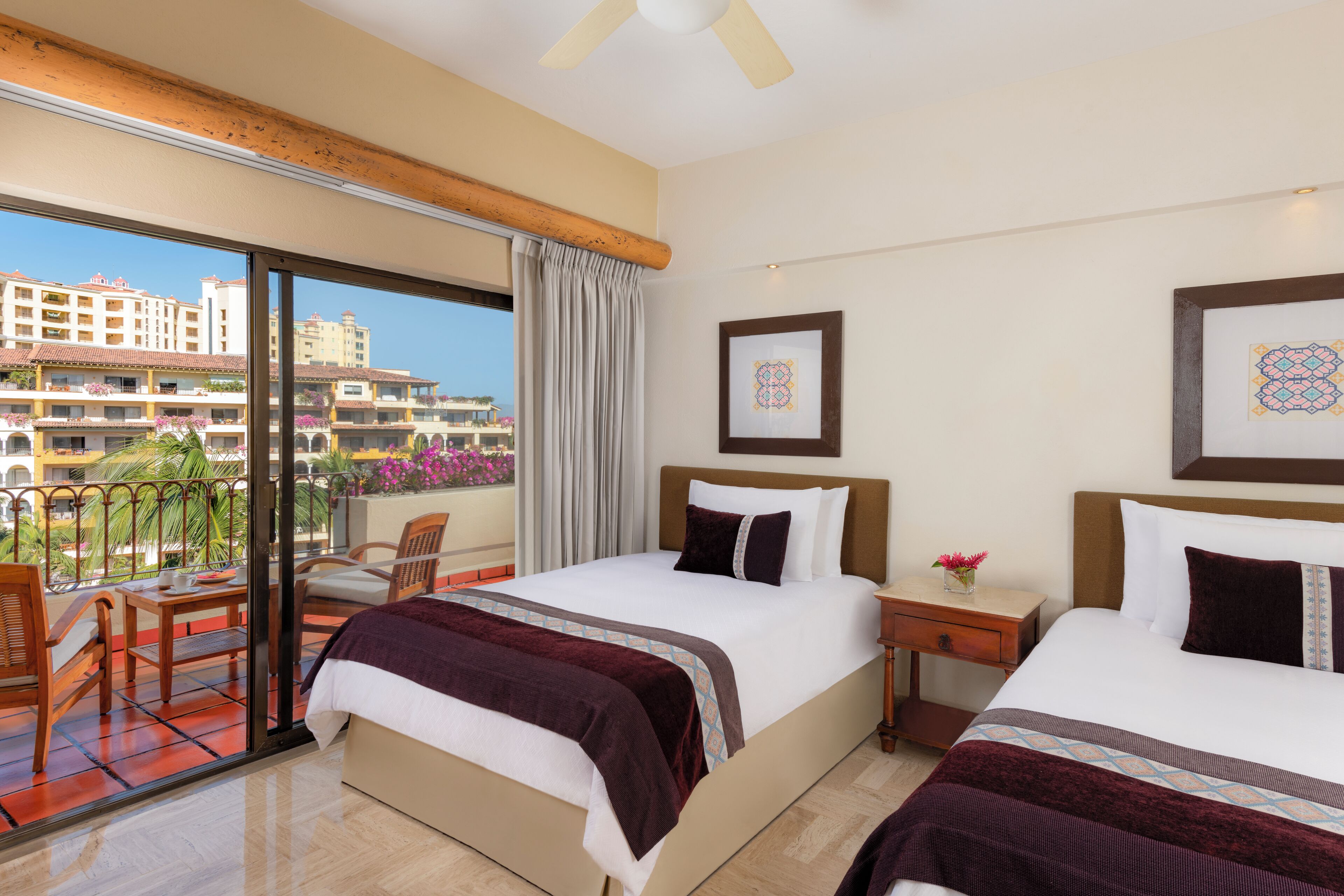 A hotel room with two beds, a balcony with a view of other buildings, and a ceiling fan.