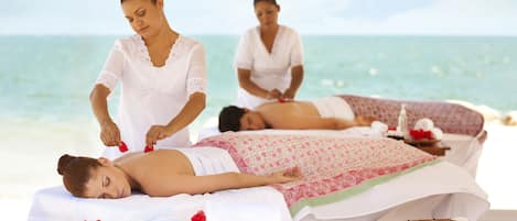 A spa setting with massage tables and a beach view.