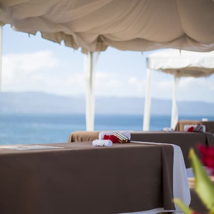 A seaside hotel room with a view of the ocean, a table with a towel and a bottle, and a canopy overhead.