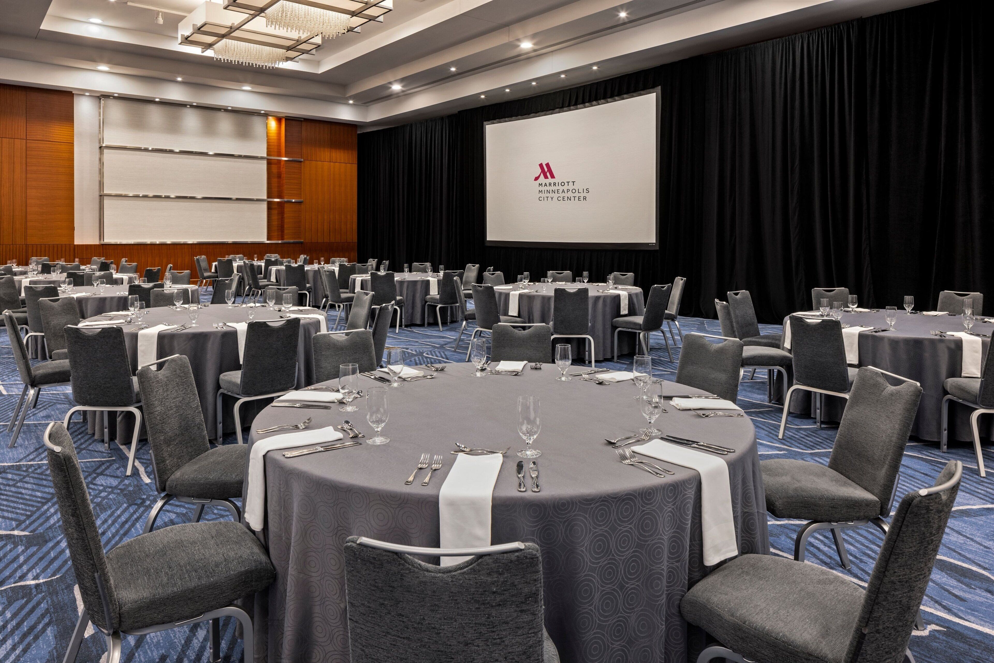 A conference room with round tables, grey chairs, and a large screen displaying the Marriott Minneapolis City Center logo.