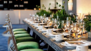 A long dining table set with plates, glasses, and cutlery, flanked by green upholstered chairs.