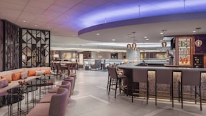 A modern hotel lobby with a curved bar area, seating arrangements, and a decorative wall.