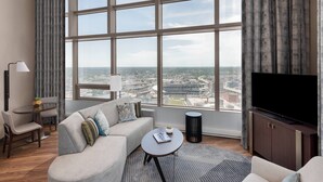 A modern living room with a large window, a sofa, a coffee table, a TV, and a small table with a lamp.