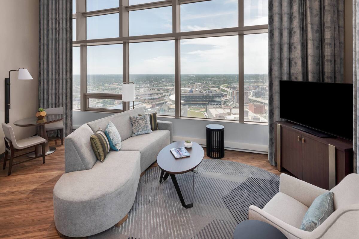 A modern living room with a large window, a sofa, a coffee table, a TV, and a small table with a lamp.
