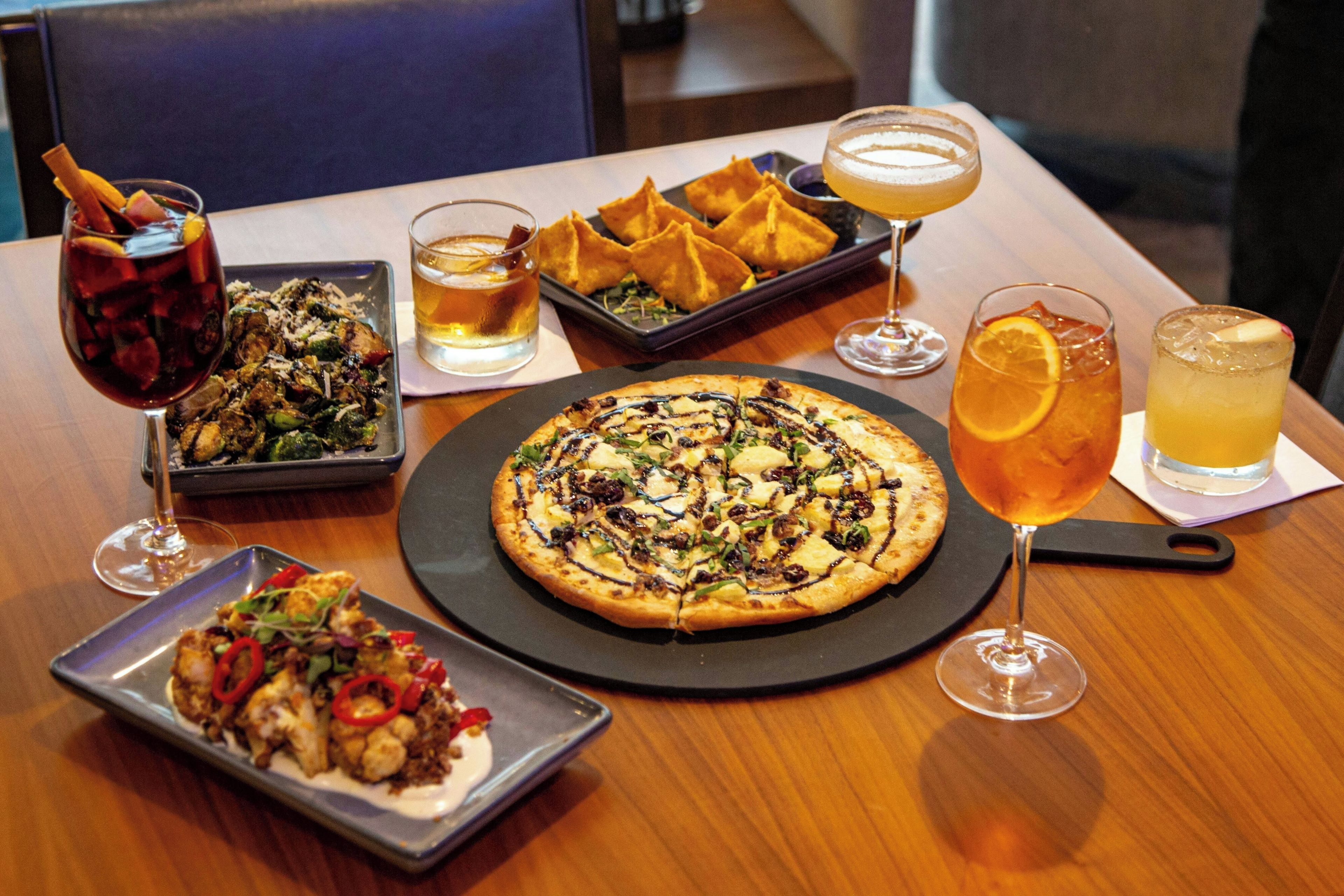 A dining table with a variety of dishes including pizza, a salad, and a dessert, accompanied by several glasses of beverages.