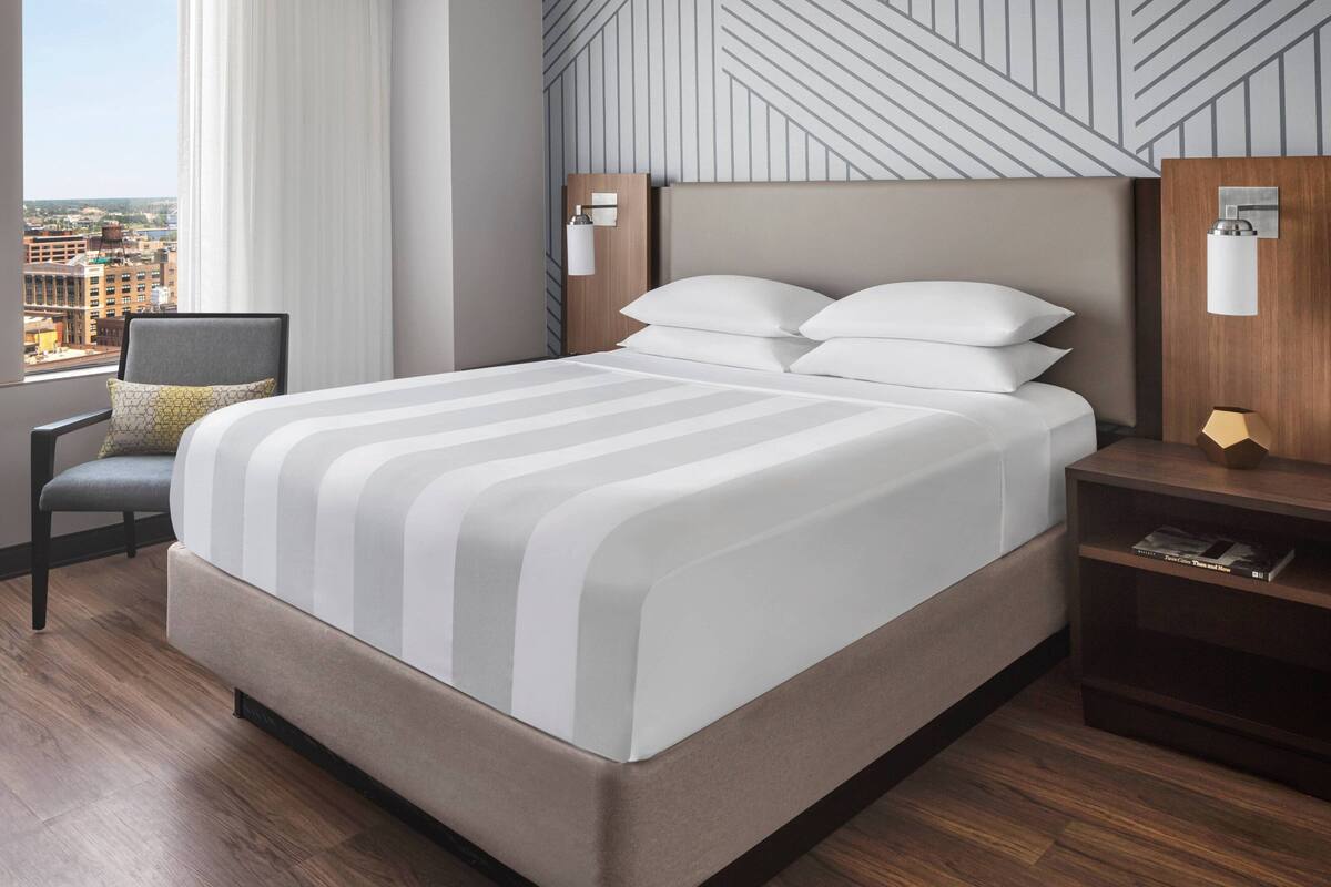 A modern hotel room with a large bed, a view of the city, and a cityscape visible through the window.
