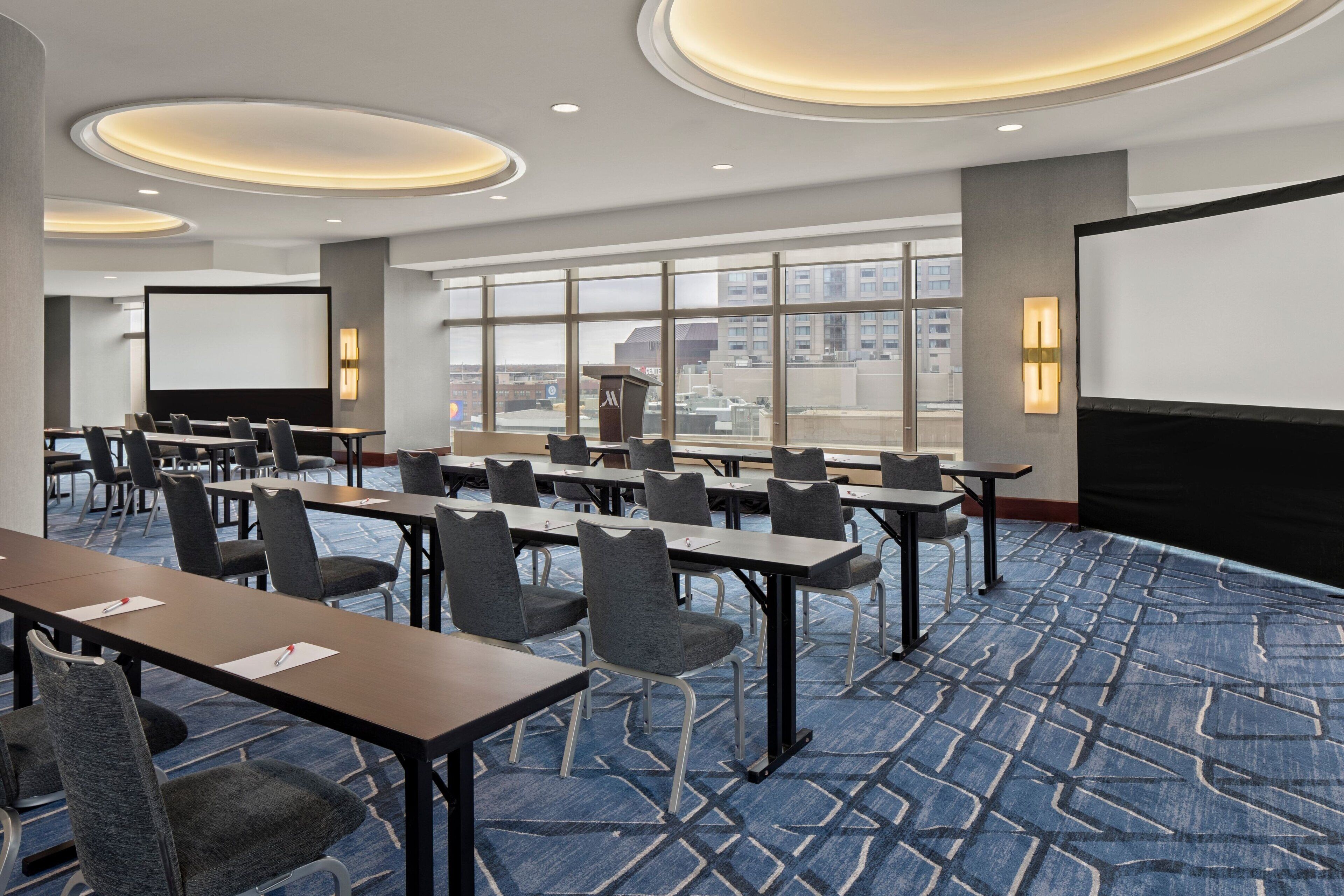 A conference room with multiple tables and chairs, large windows, and a projection screen.
