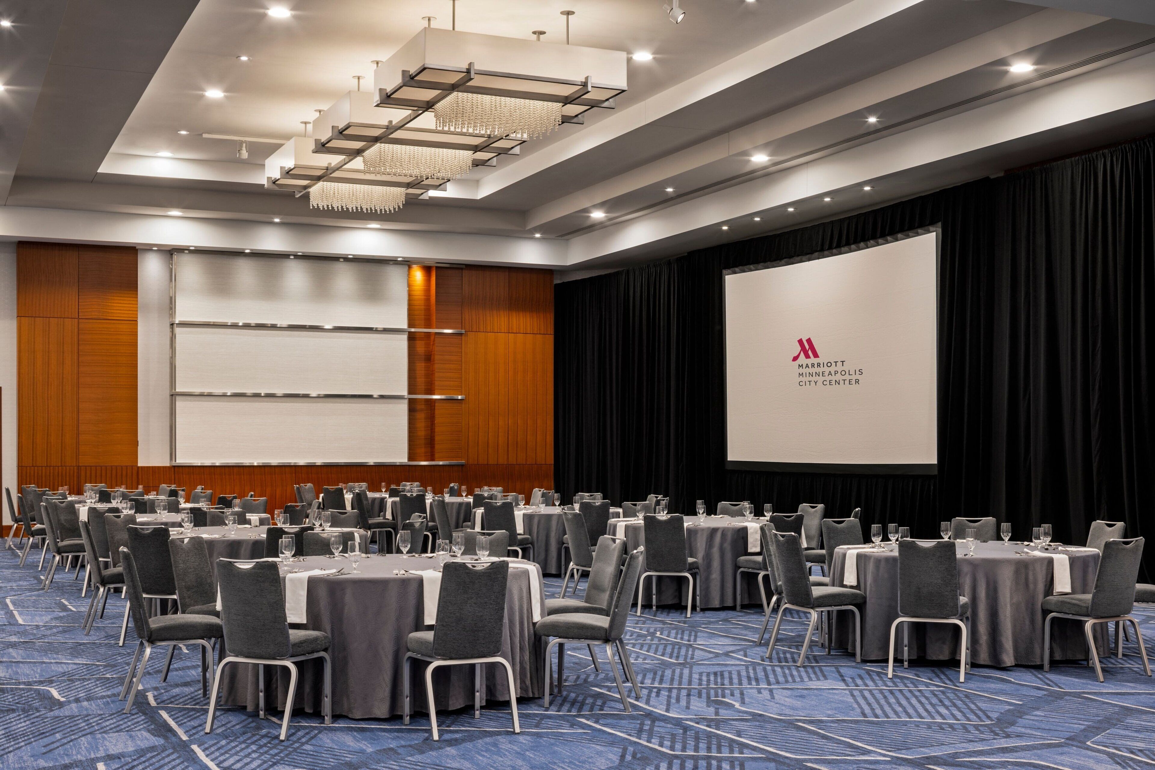 Un salón de conferencias con varias mesas y sillas, una pantalla grande y una araña.