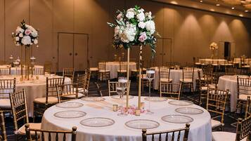 A banquet hall with round tables, gold chairs, and floral centerpieces.