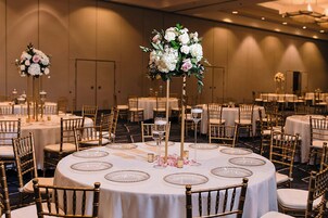 A banquet hall with round tables, gold chairs, and floral centerpieces.