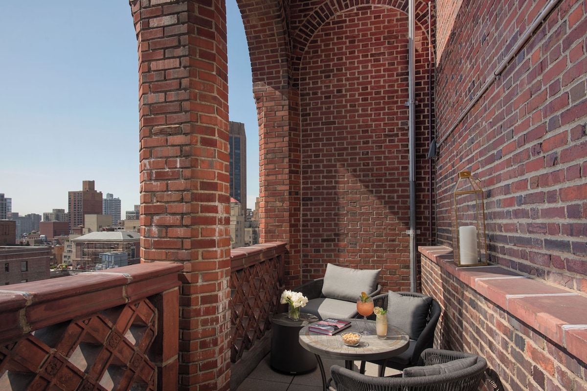 A balcony with brick walls, a table with a drink, and a chair.