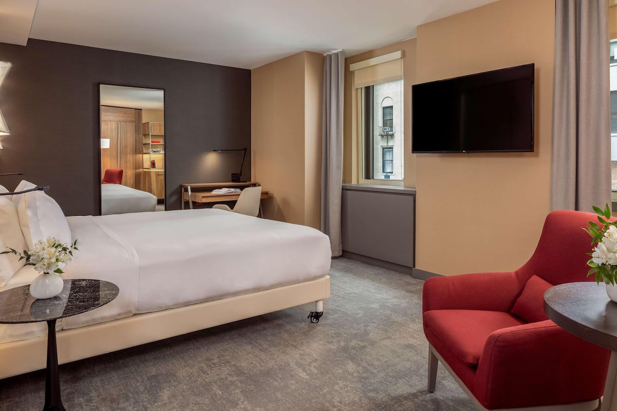 Ein Hotelzimmer mit einem Bett, einem Schreibtisch, einem Sessel, einem Fernseher und einem Fenster.