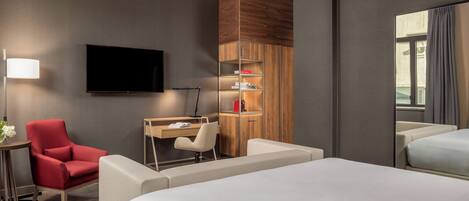 Una habitación de hotel con una cama, un escritorio, un sillón rojo, un televisor y un armario.