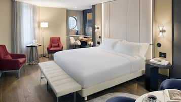 Une chambre d’hôtel avec un grand lit, un bureau, une chaise, un banc et une petite table sur laquelle se trouvent une tasse et un livre.