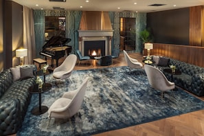 Een luxe woonkamer met een vleugelpiano, zachte zithoek, een open haard en een groot tapijt.