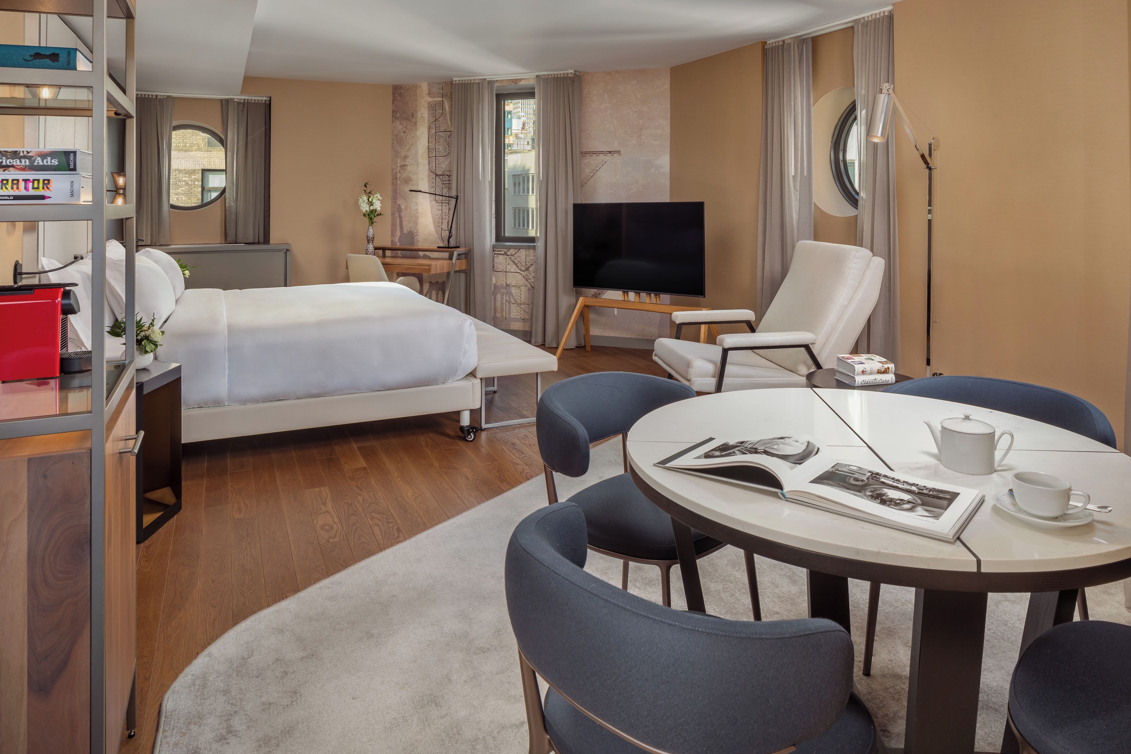 A hotel room with a bed, a desk, a TV, a chair, a table, and a bookshelf.
