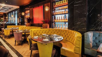 A restaurant interior with yellow booths, round tables, and a wine display.