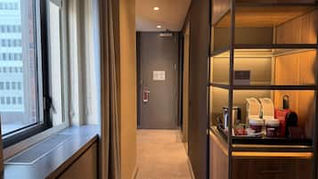 A hotel corridor with a window, a door, and a kitchenette area with coffee makers and a kettle.