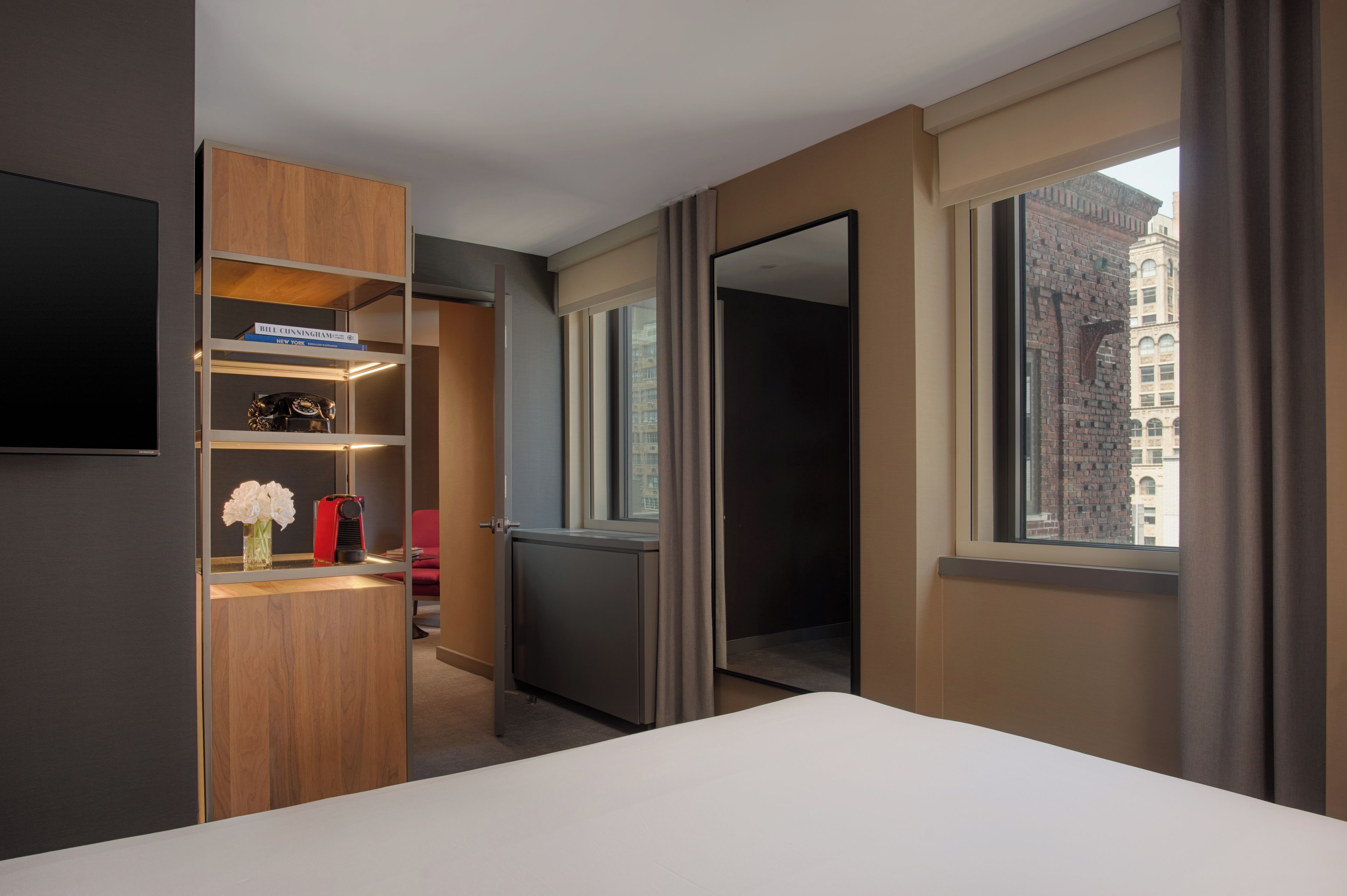 Habitación de hotel con cama, armario, espejo y ventana con vista a la ciudad.