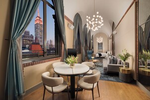 A hotel room with a city skyline view, a round dining table with chairs, a sofa, and a chandelier.