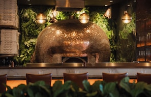 A restaurant interior with a brick oven, hanging lights, and a menu board. - NH Collection New York Madison Avenue (New York)