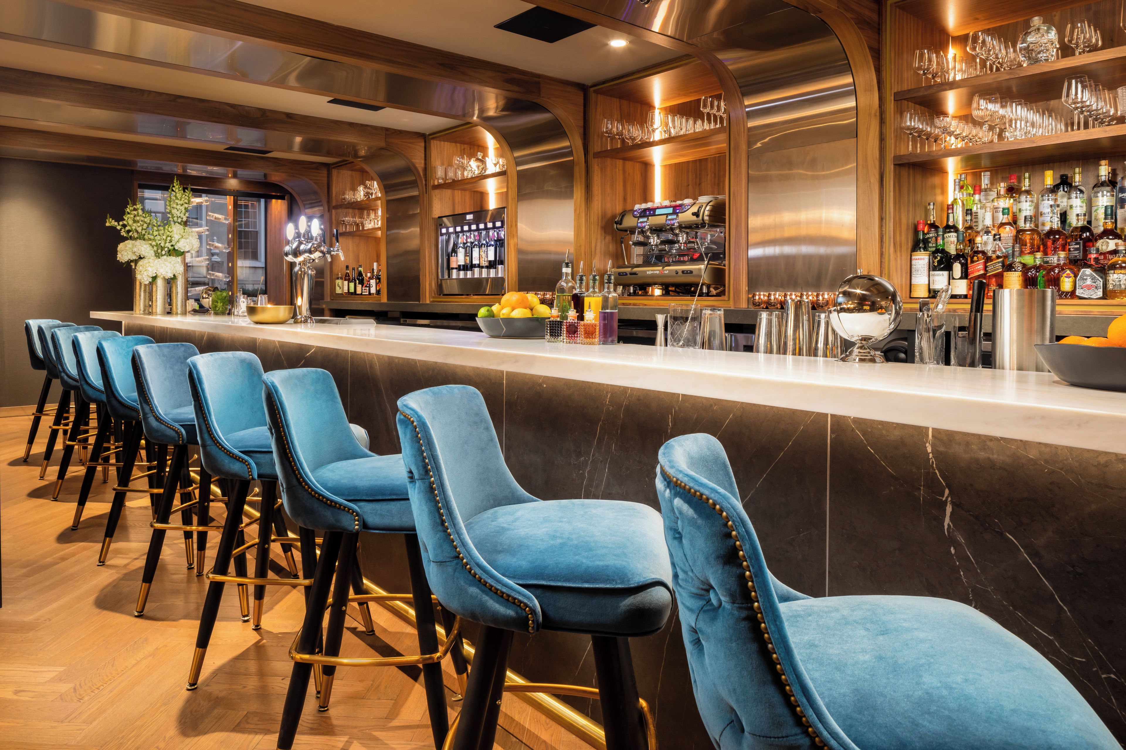 A bar area with a row of blue barstools, a bar counter, and a variety of bottles and glasses.