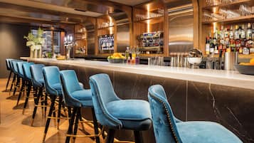 A bar area with a row of blue barstools, a bar counter, and a variety of bottles and glasses.
