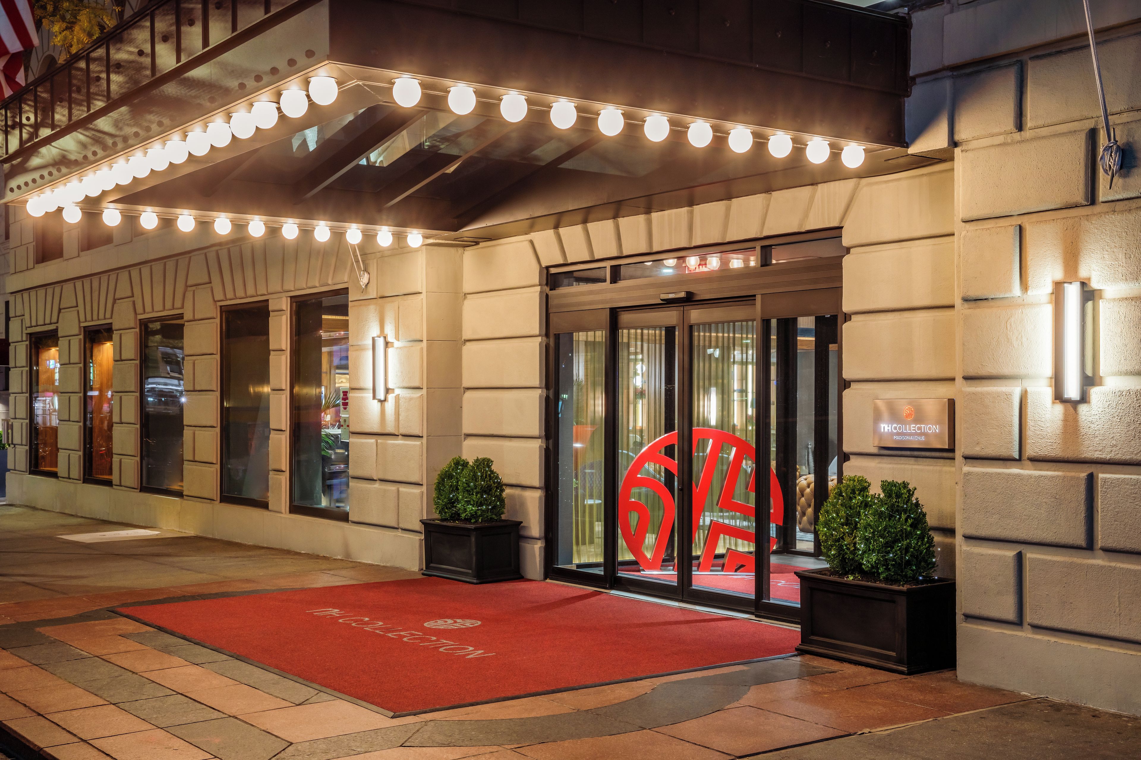 A hotel entrance with a red carpet, a large illuminated number '6' sign, and a glass door.