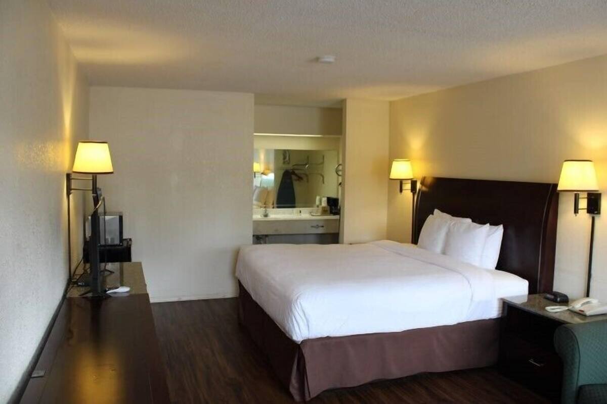 A hotel room with a large bed, bedside lamps, a small desk with a telephone, and a mirror above the bed.