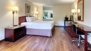 Una camera d'albergo con un letto, abat-jour, una scrivania con una sedia, uno specchio e un comò.