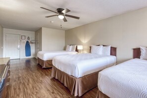 A hotel room with two beds, a ceiling fan, a door, and a blue surfboard on the wall.