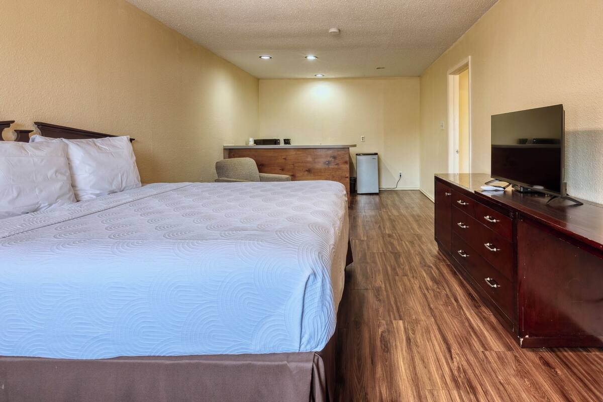 A hotel room with a bed, a dresser, a television, and a kitchenette area.