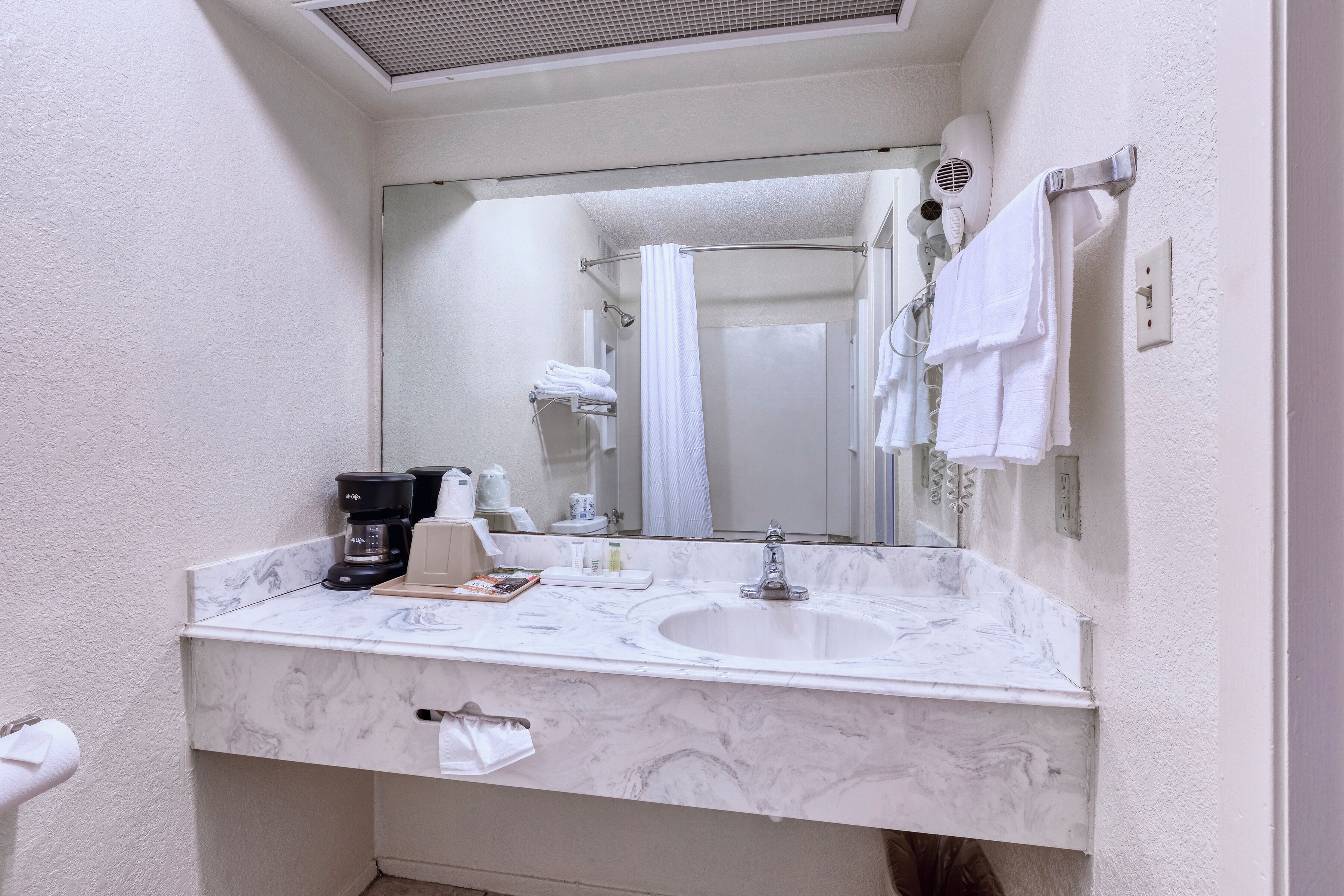 Un baño con lavamanos de mármol, un espejo, un secador de pelo y un perchero para toallas.